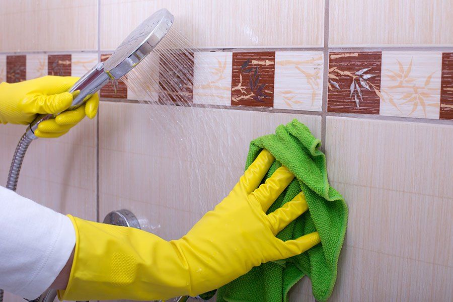 Une personne avec des gants jaunes rince le carrelage d'une cabine de douche