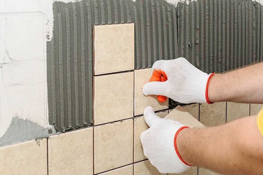Un homme est en train de poser du carrelage de forme carrée au mur