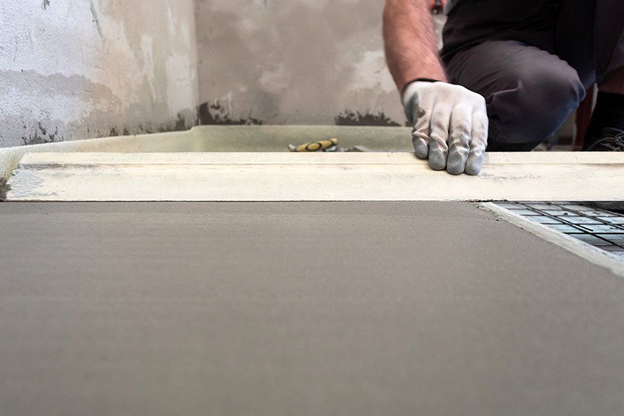 Un ouvrier lisse une chape avec une lambourde de bois