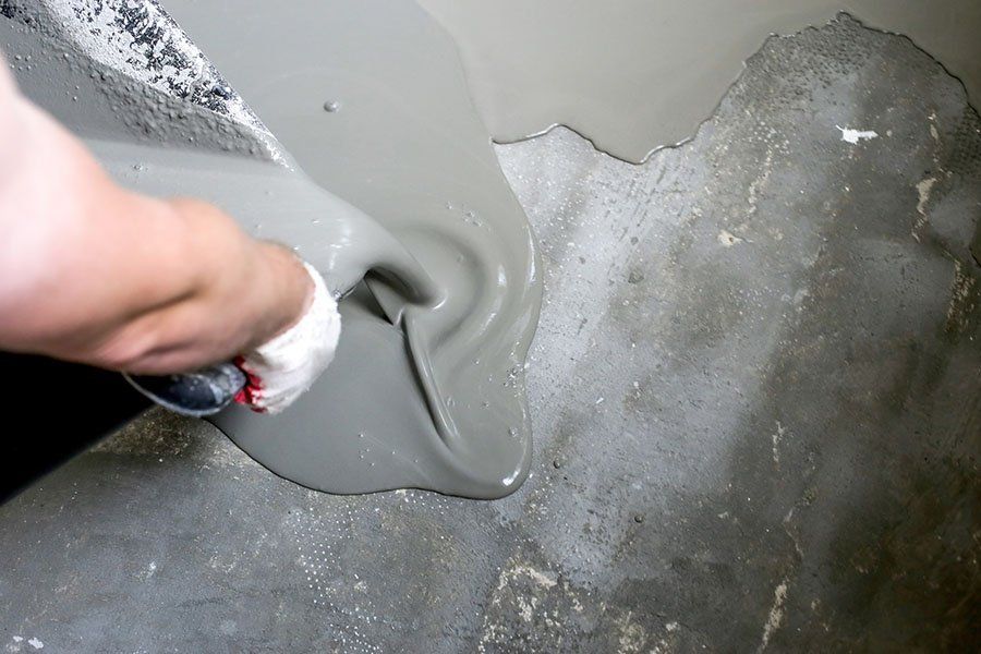 Une personne verse une chape liquide sur une dalle en béton