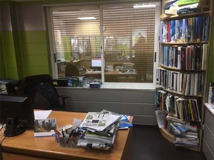 Una oficina desordenada con un escritorio, una computadora, estanterías y una ventana.