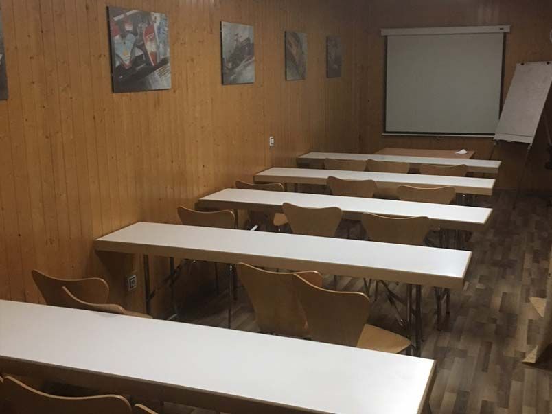 Un aula con mesas y sillas y una pantalla de proyección.