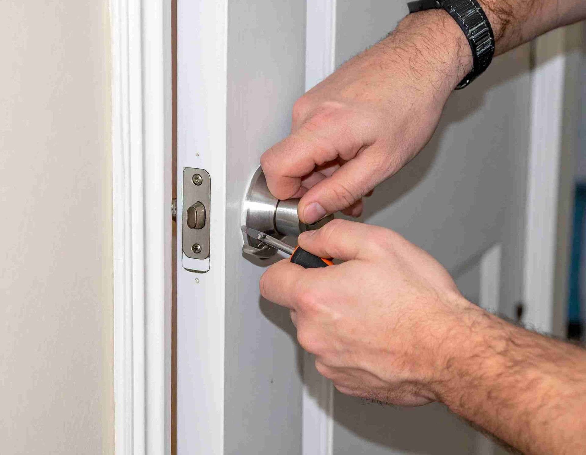 Persona que utiliza un destornillador para instalar un pomo en una puerta blanca.