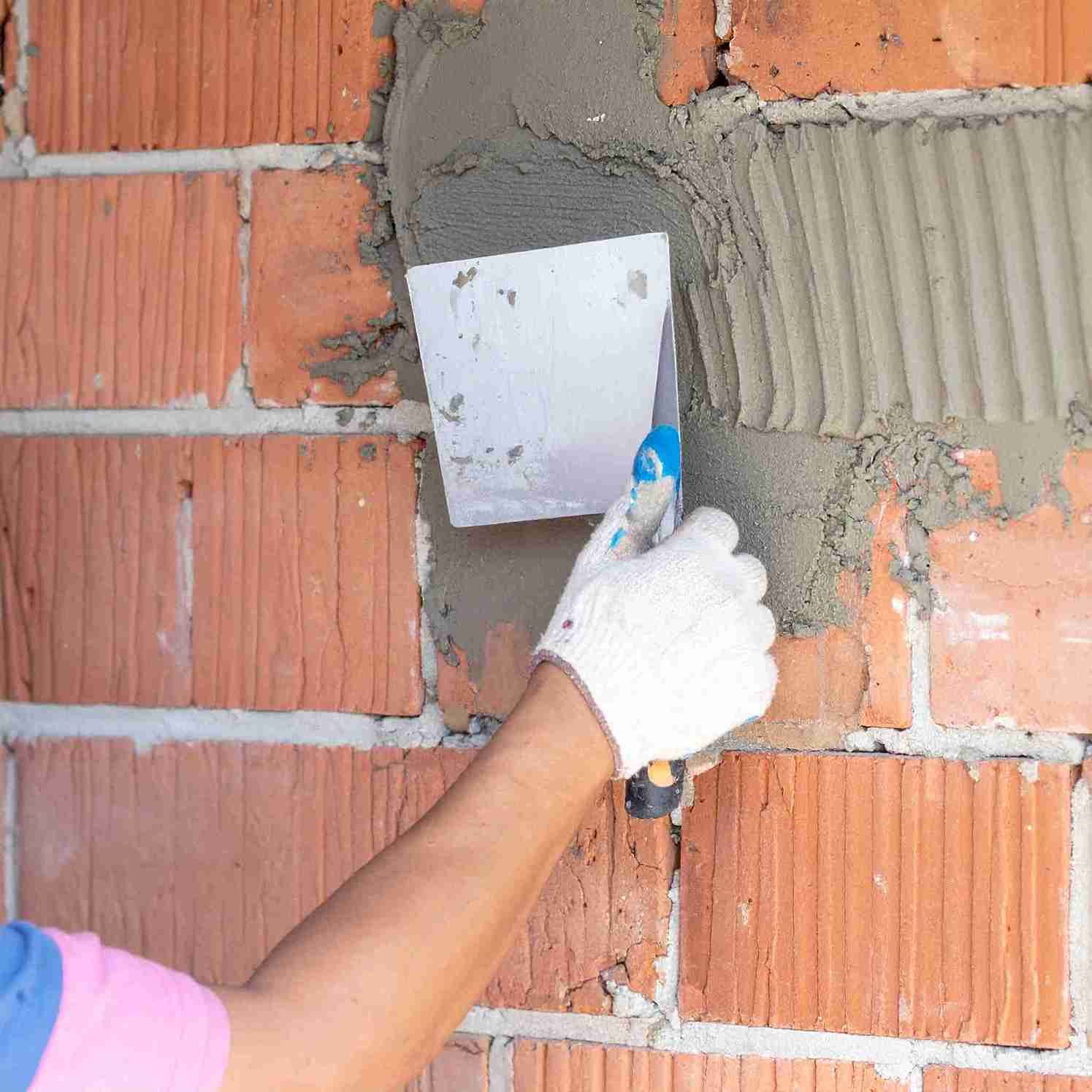 Persona que utiliza una paleta para aplicar mortero a una pared de ladrillos rojos.