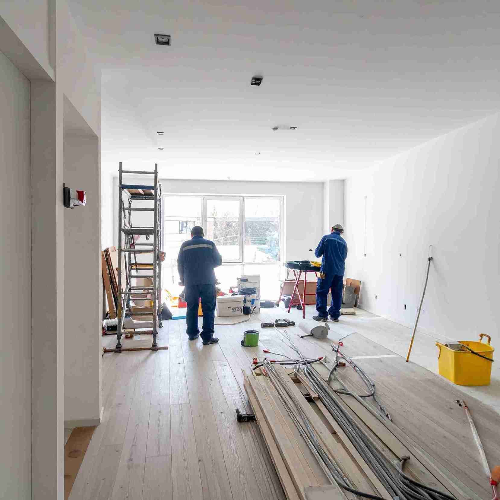 Dos trabajadores en una habitación en remodelación con herramientas, una escalera y materiales de construcción.