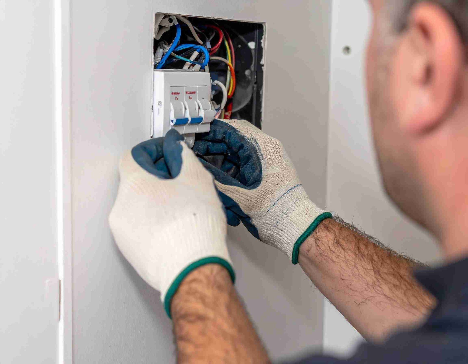 Hombre instalando cableado eléctrico, con guantes, en una caja montada en la pared.