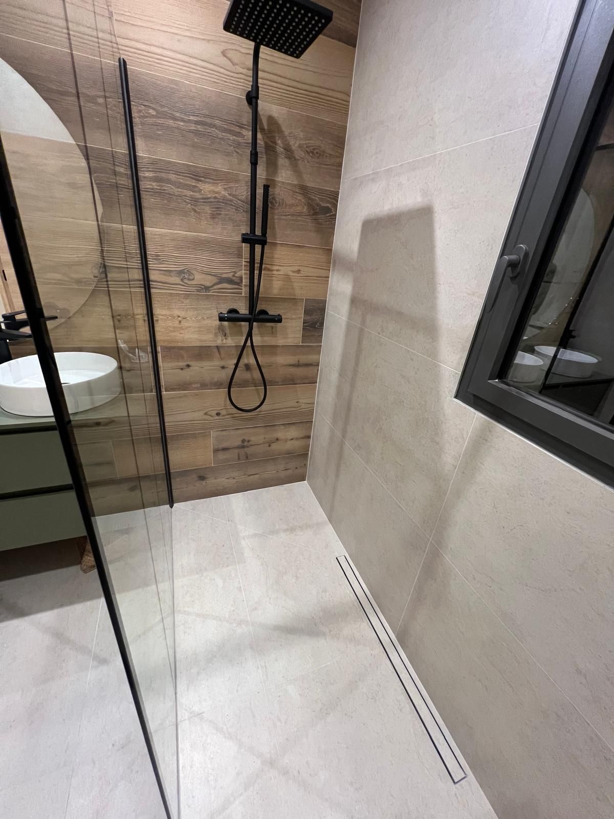Salle de bains moderne avec douche, carrelage imitation bois et bonde rectangulaire.