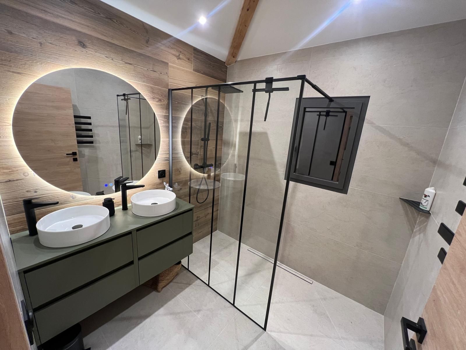 Salle de bains moderne avec meuble-lavabo double vasque, douche et miroirs ronds avec éclairage.