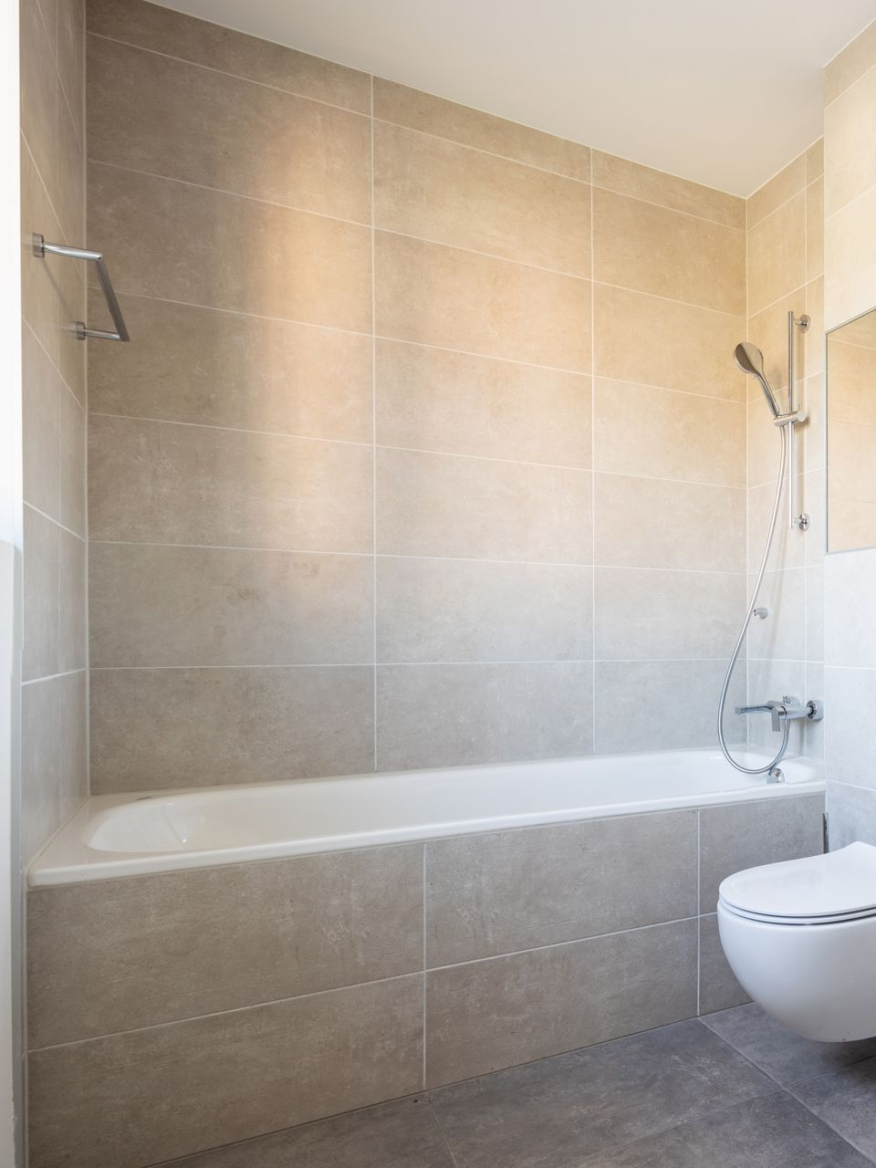 Salle de bains avec murs carrelés, baignoire blanche, toilettes et pommeau de douche.