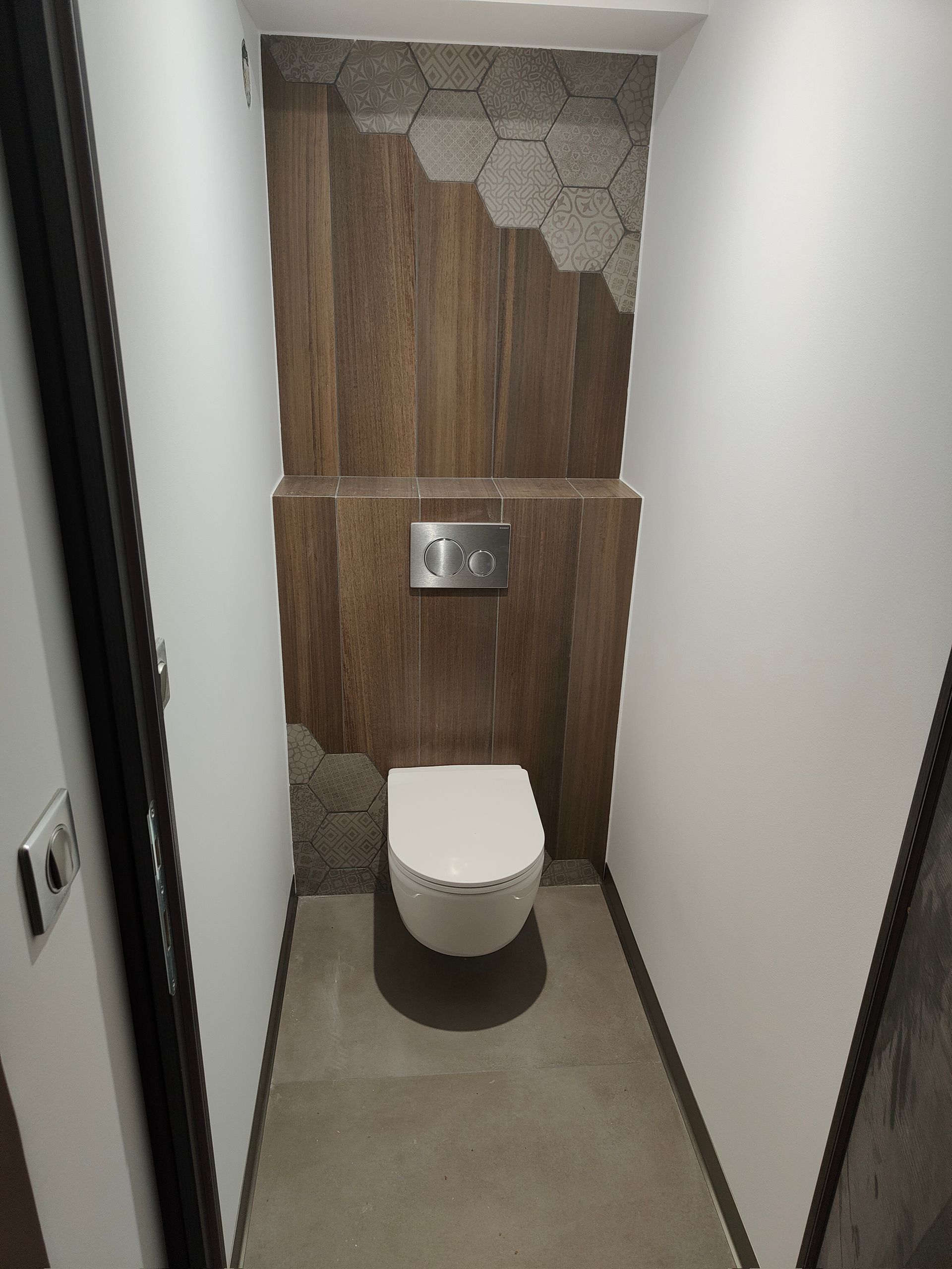 Petite salle de bains avec toilettes blanches, accents muraux en bois et en pierre hexagonale.