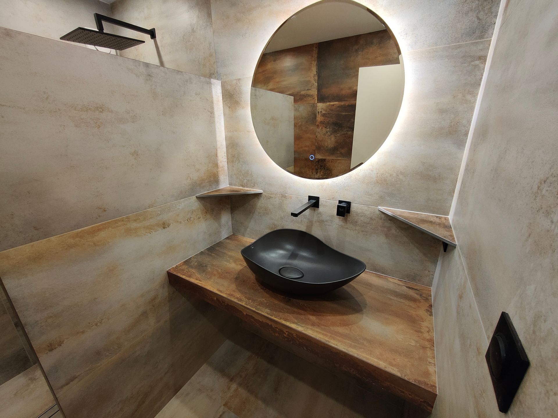 Salle de bains avec miroir rond, vasque noire et murs texturés beige clair.