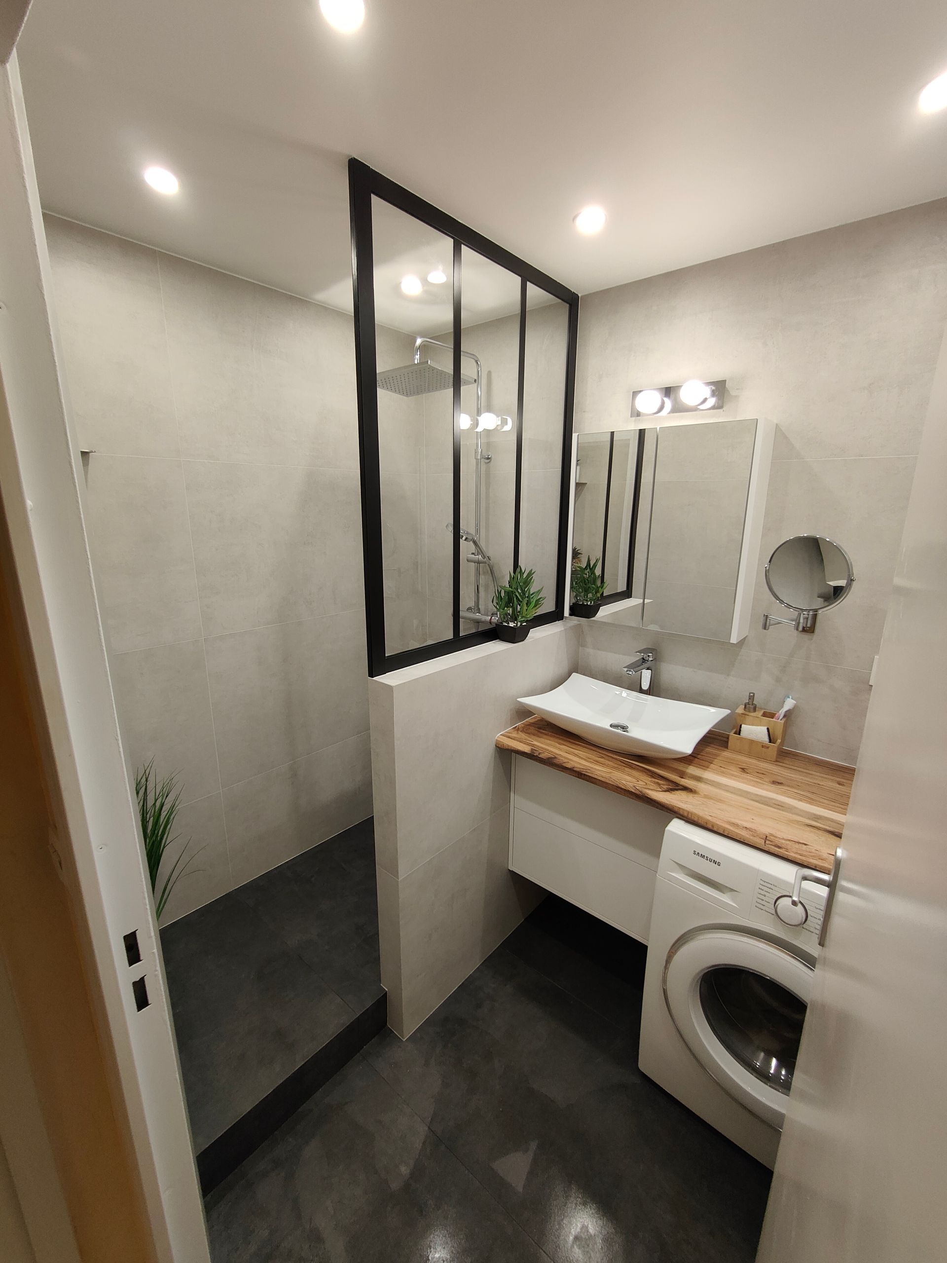 Petite salle de bains moderne avec douche à l'italienne, lavabo et lave-linge. Dominée par les tons gris et blancs.