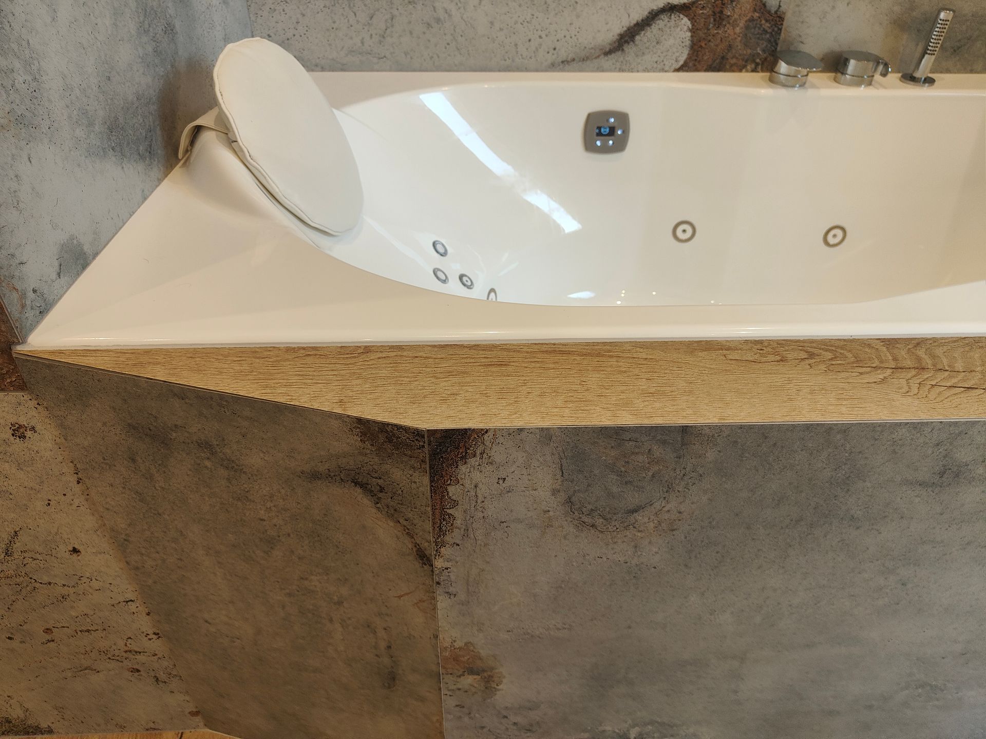 Baignoire jacuzzi blanche encastrée dans un socle en béton texturé gris avec appui-tête.