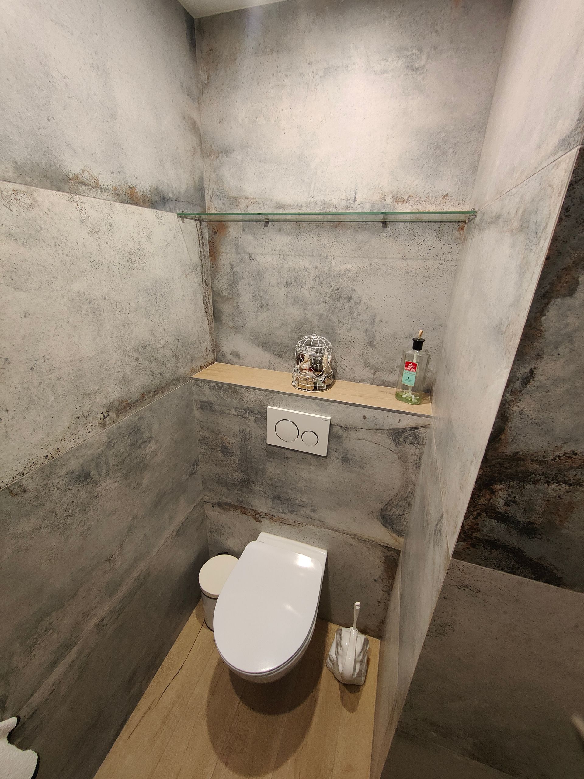 Petite salle de bains avec murs en béton, toilettes, étagère avec objets de décoration et articles de toilette.