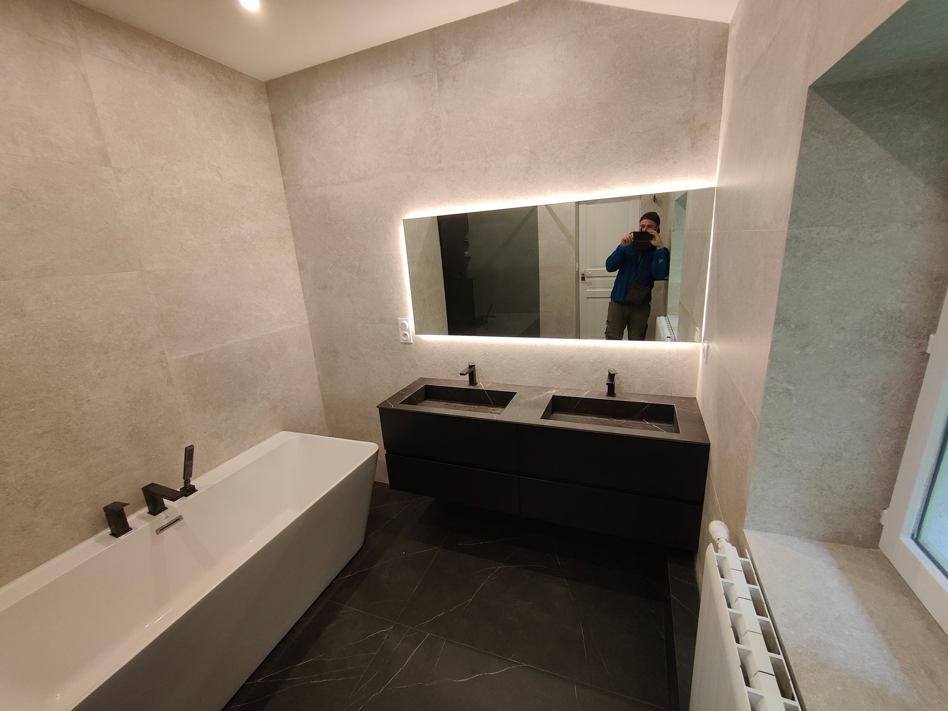 Salle de bains moderne avec meuble-lavabo noir, baignoire blanche et grand miroir avec éclairage LED.