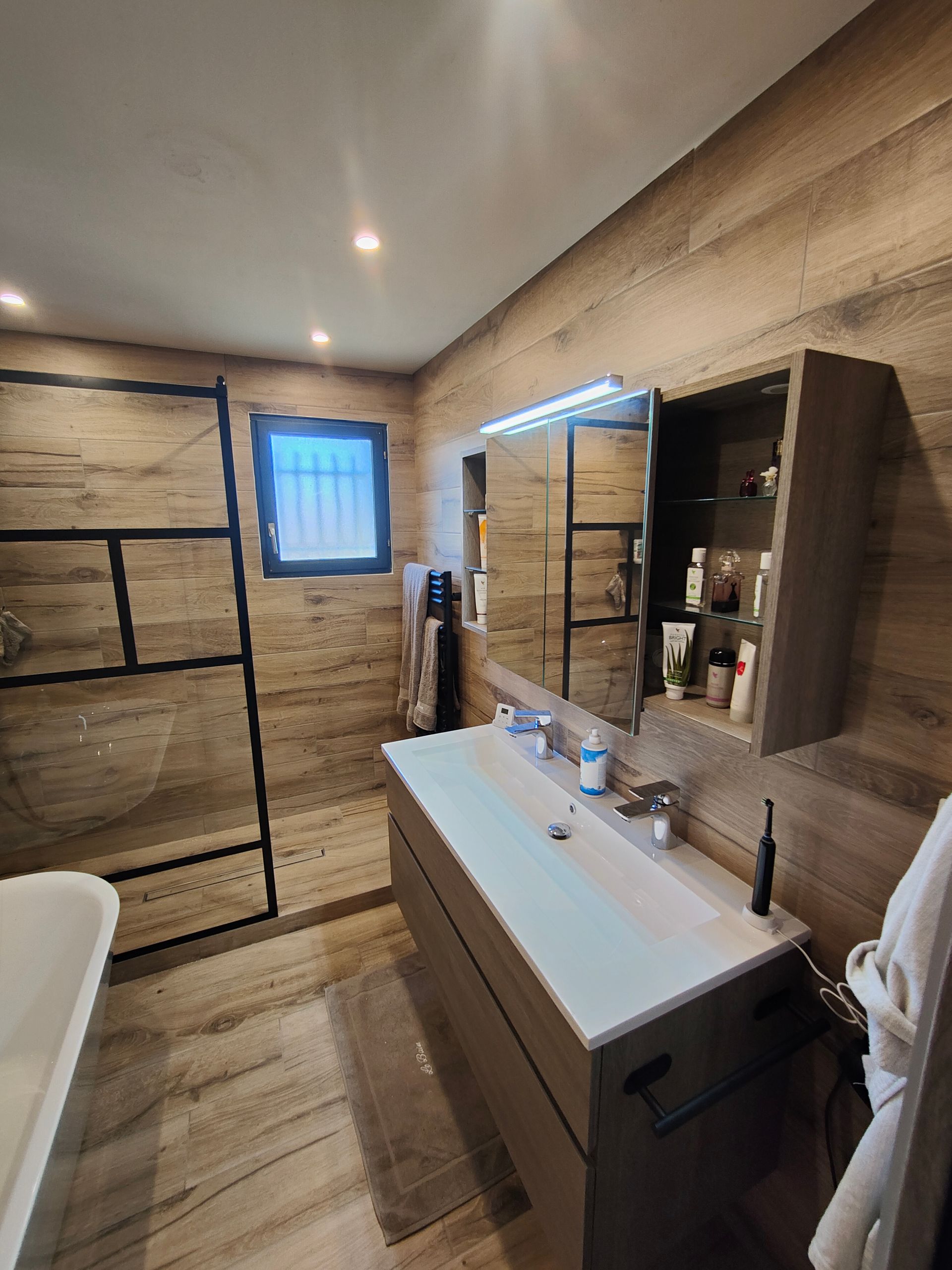 Salle de bains avec murs en bois, lavabo, armoire de toilette avec miroir et cabine de douche en verre.