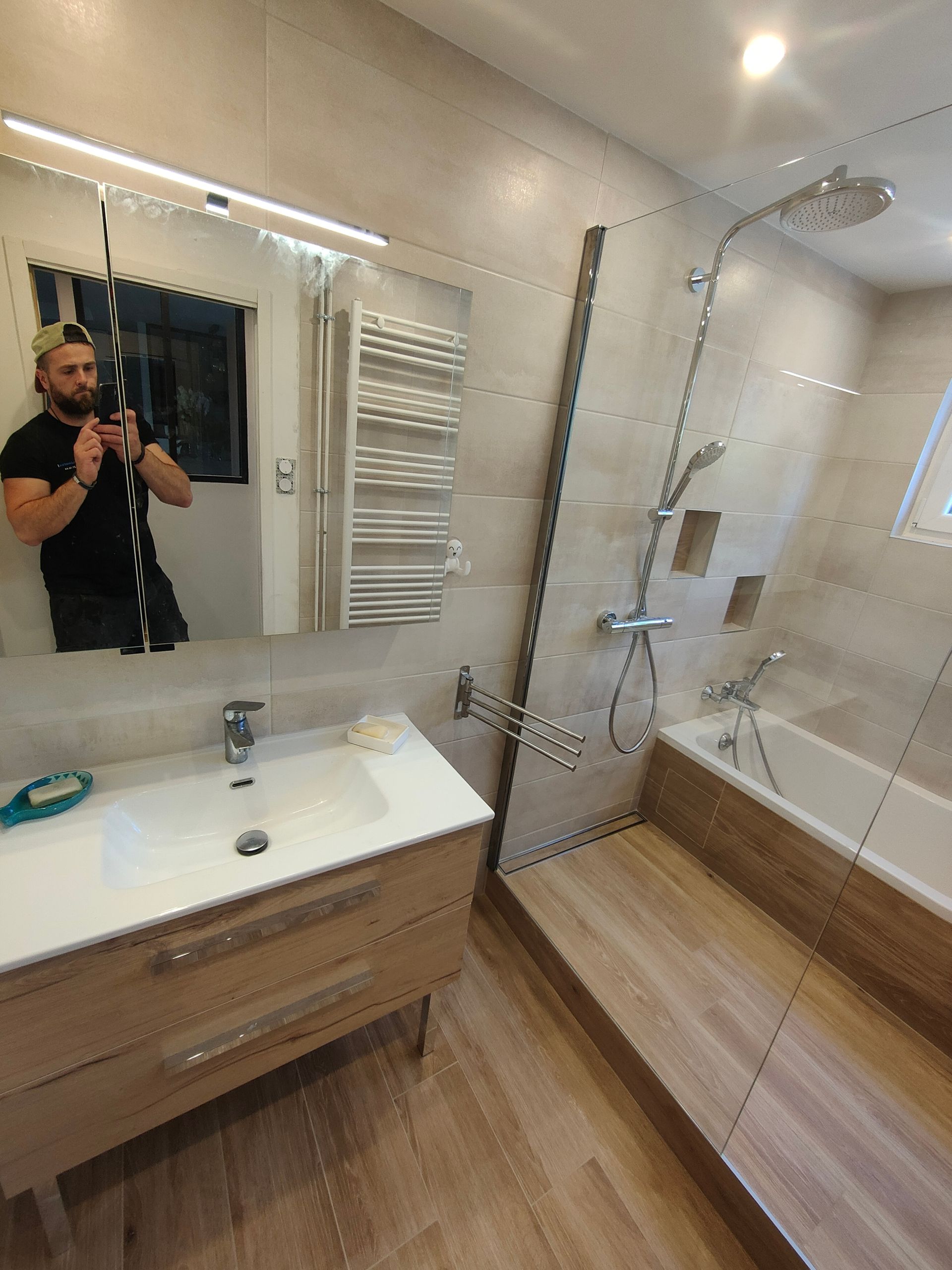 Salle de bains avec douche en verre, carrelage gris, sol à motifs et toilettes blanches.