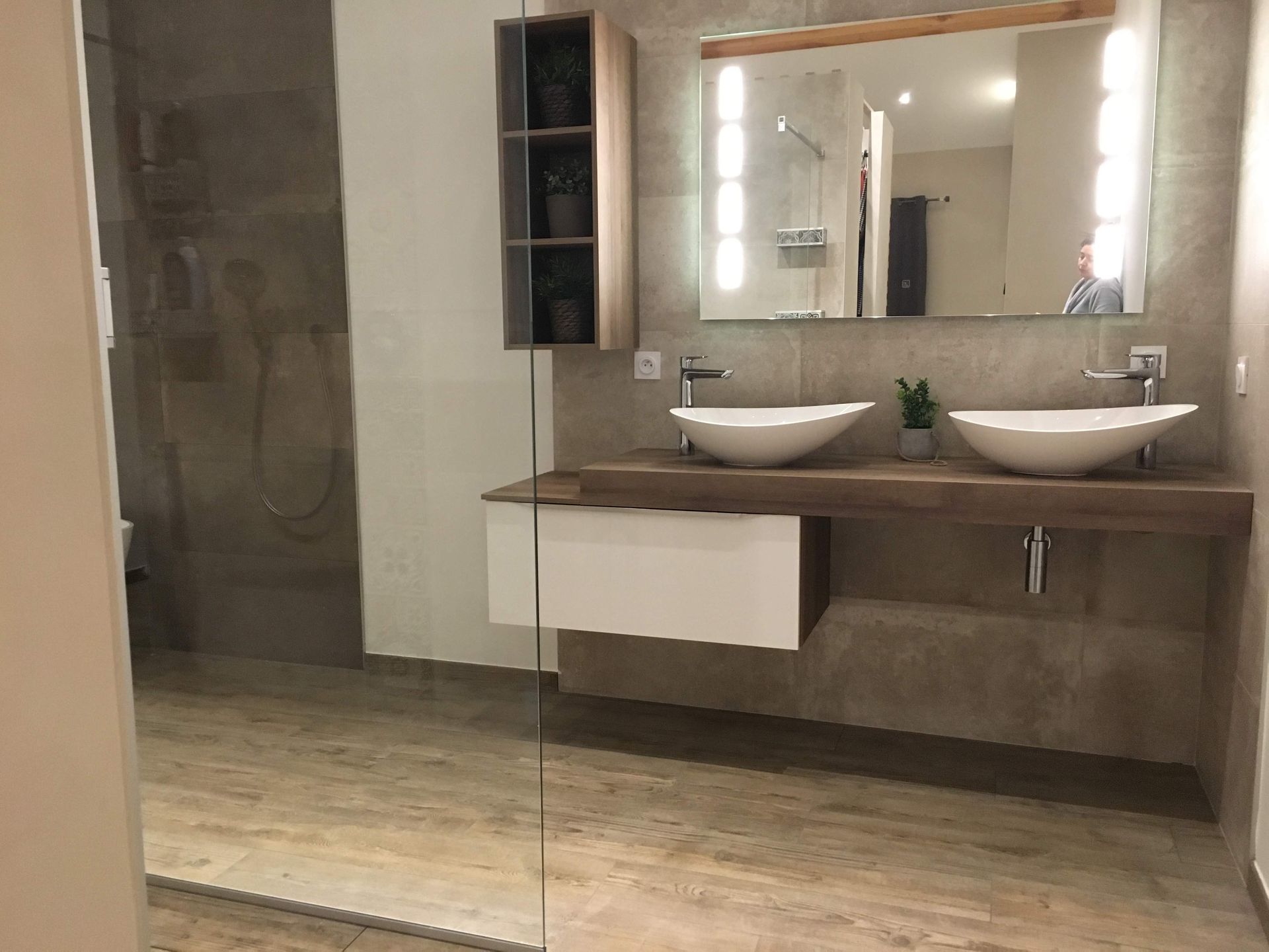Salle de bains moderne avec double vasque, grand miroir avec éclairage, comptoir en bois, douche et meuble suspendu.