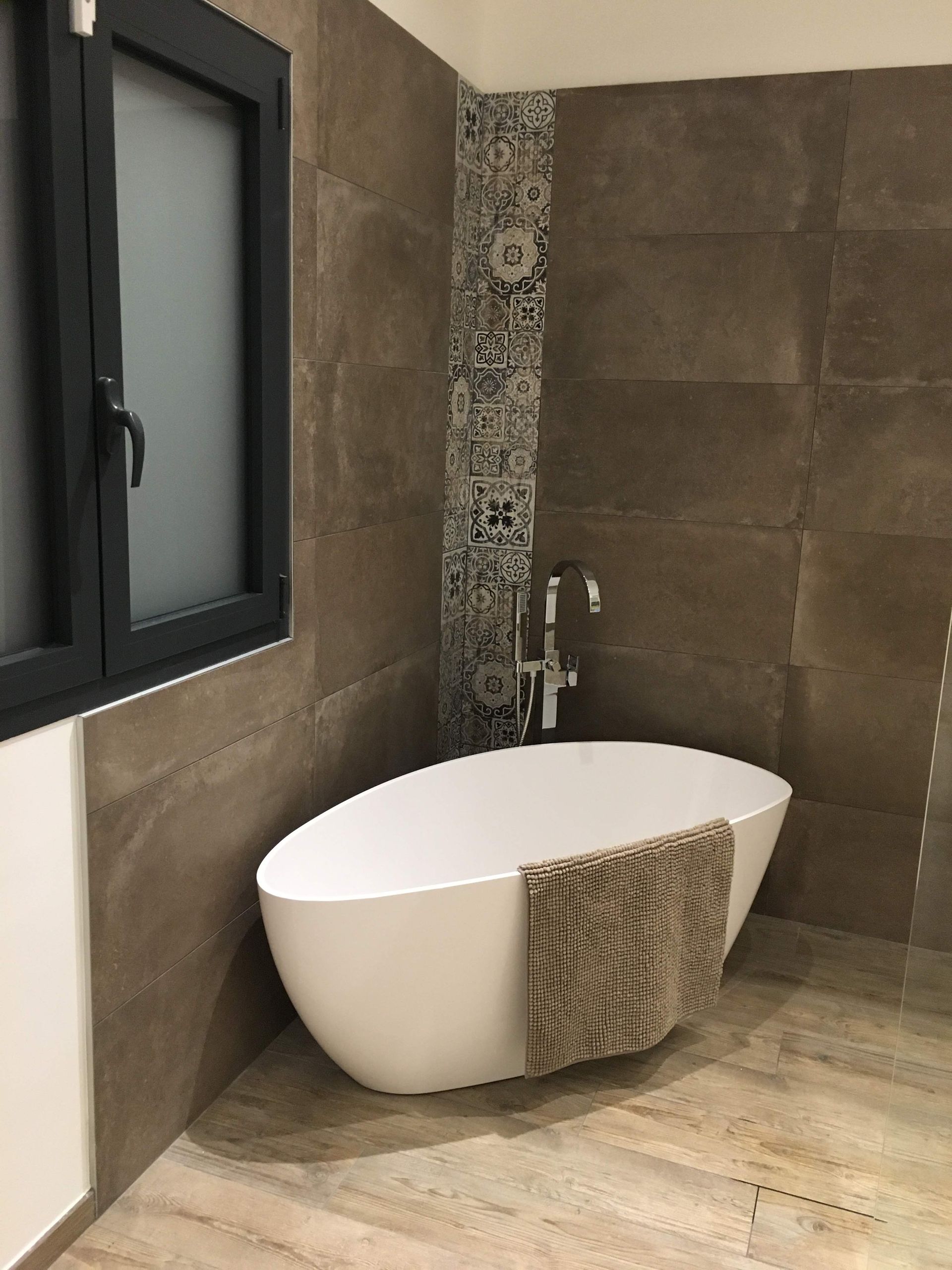 Salle de bains moderne avec baignoire ovale blanche, murs carrelés marron et éléments décoratifs à motifs.