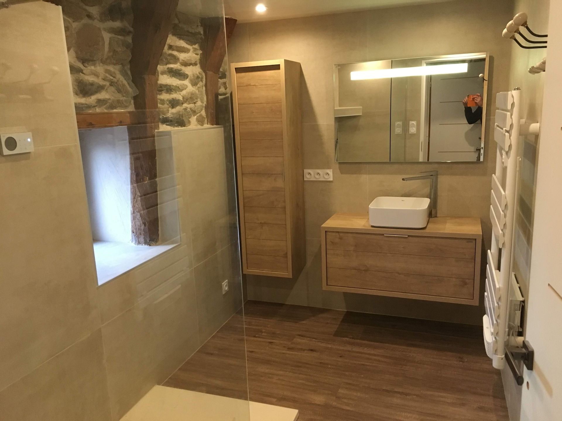 Salle de bains moderne avec meubles en bois, lavabo, miroir et mur en pierre.