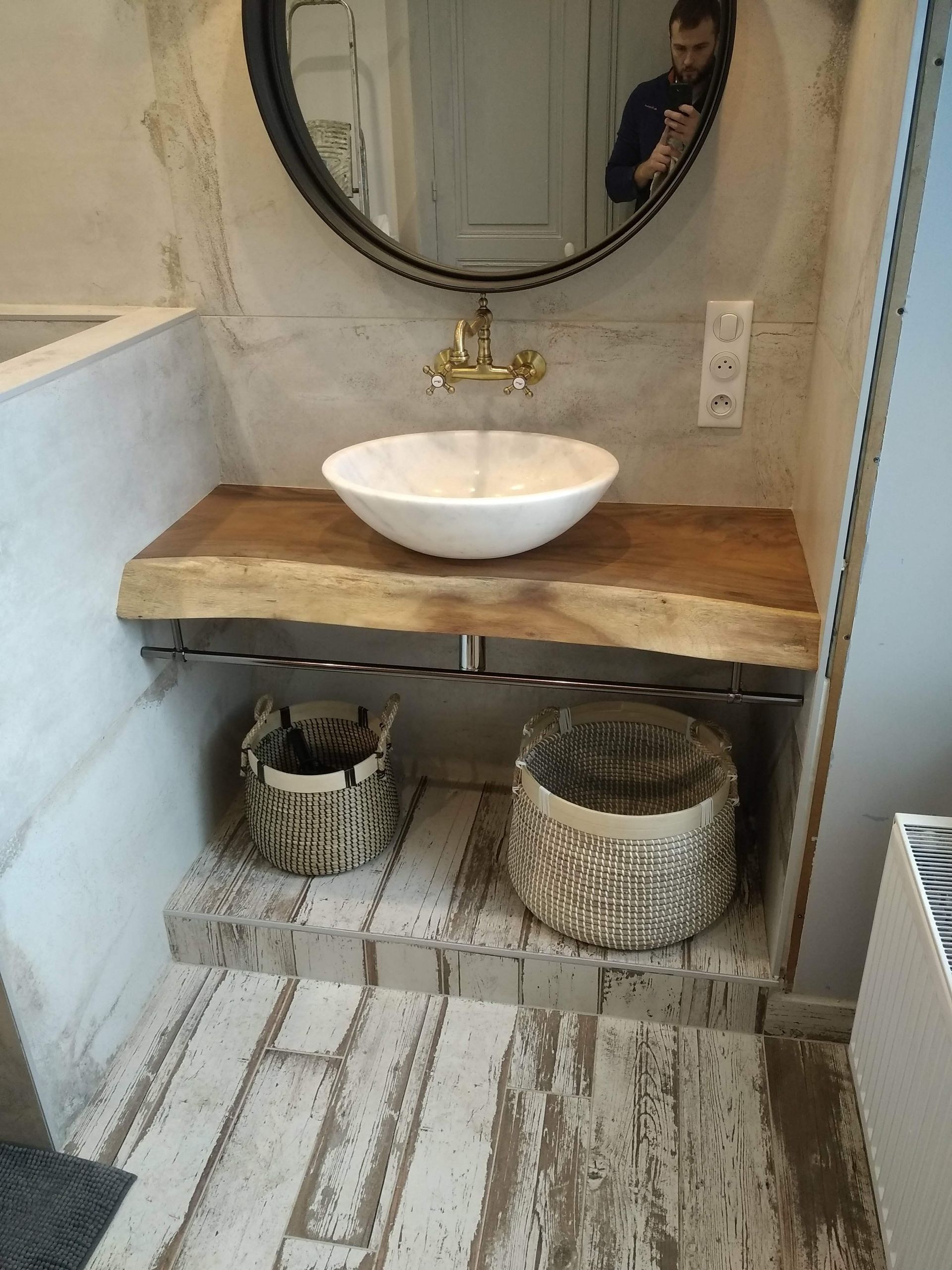 Salle de bains avec lavabo blanc sur un plan de travail en bois, paniers en dessous, miroir rond.