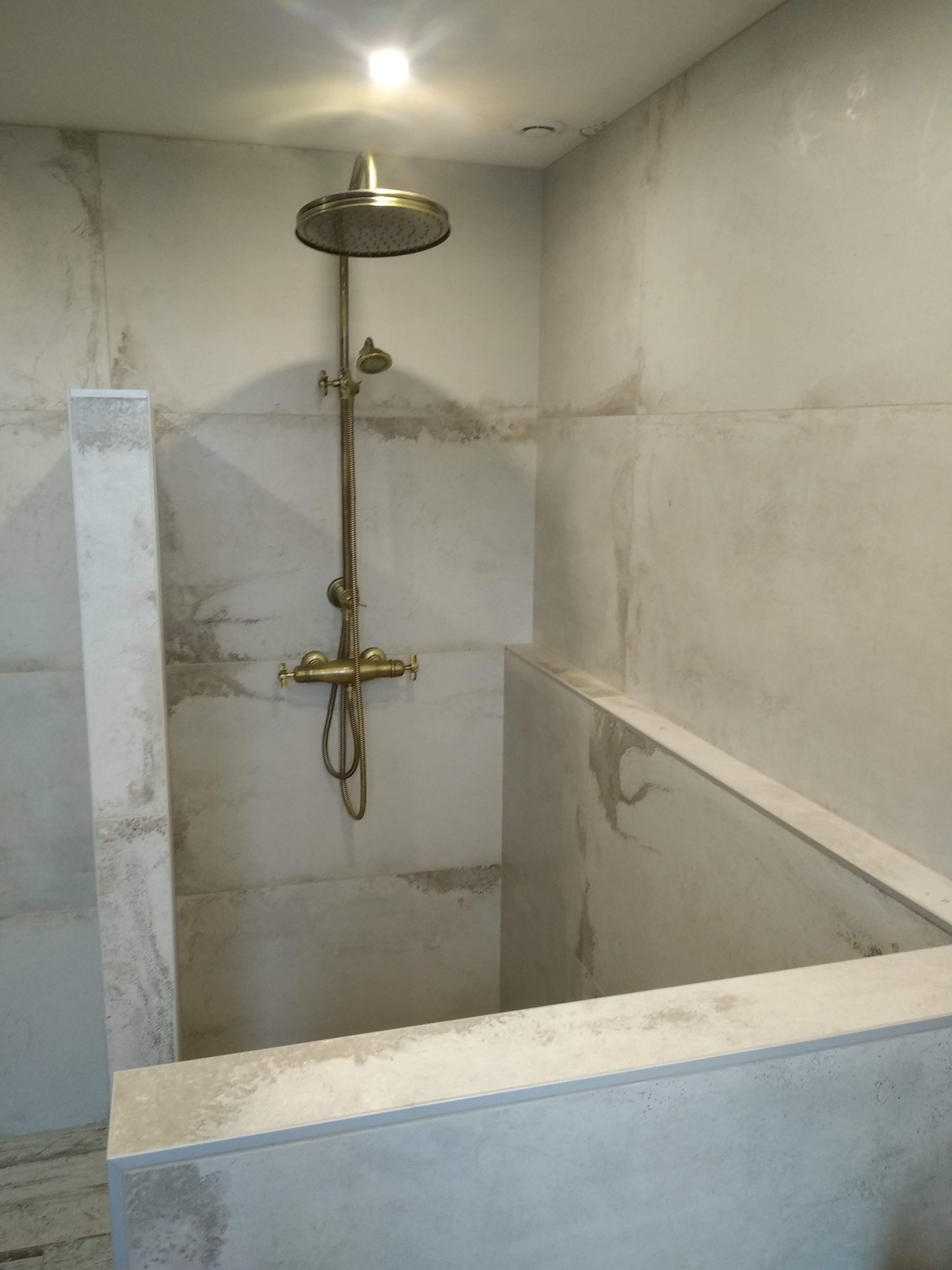 Une douche moderne avec robinetterie en bronze et murs carrelés gris clair.