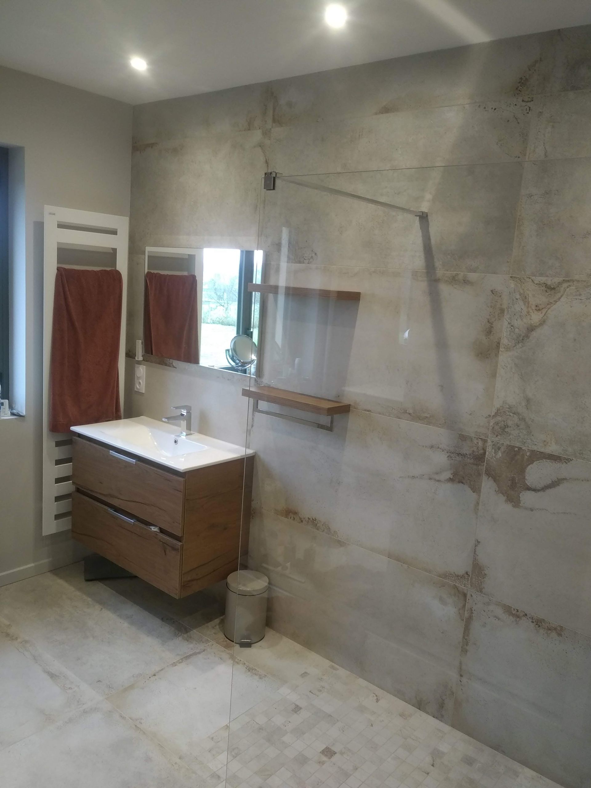 Salle de bains avec meuble-lavabo en bois, murs carrelés grand format, douche en verre et sèche-serviettes.