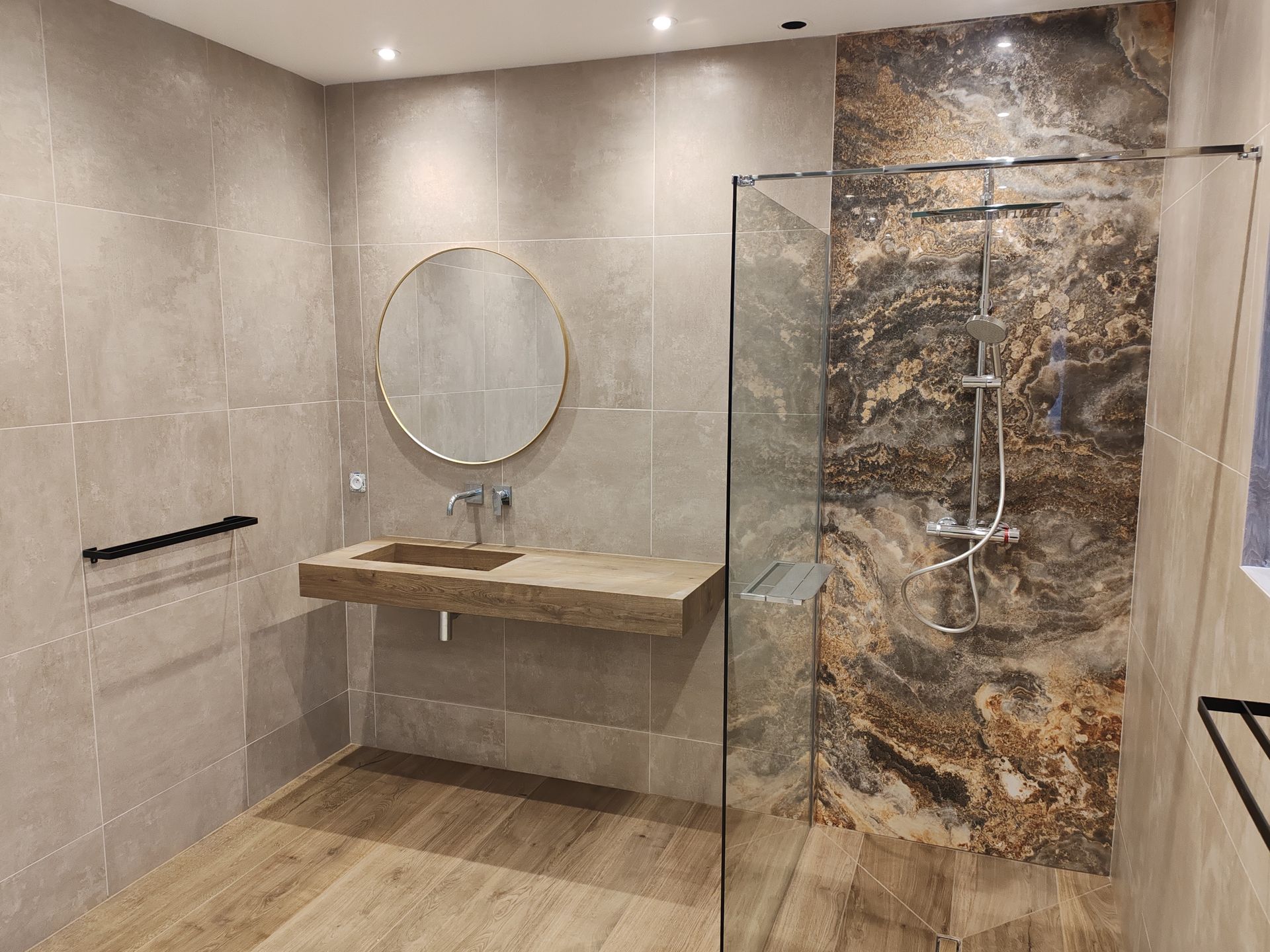 Salle de bains moderne aux tons neutres, mur en pierre, lavabo suspendu et cabine de douche en verre.