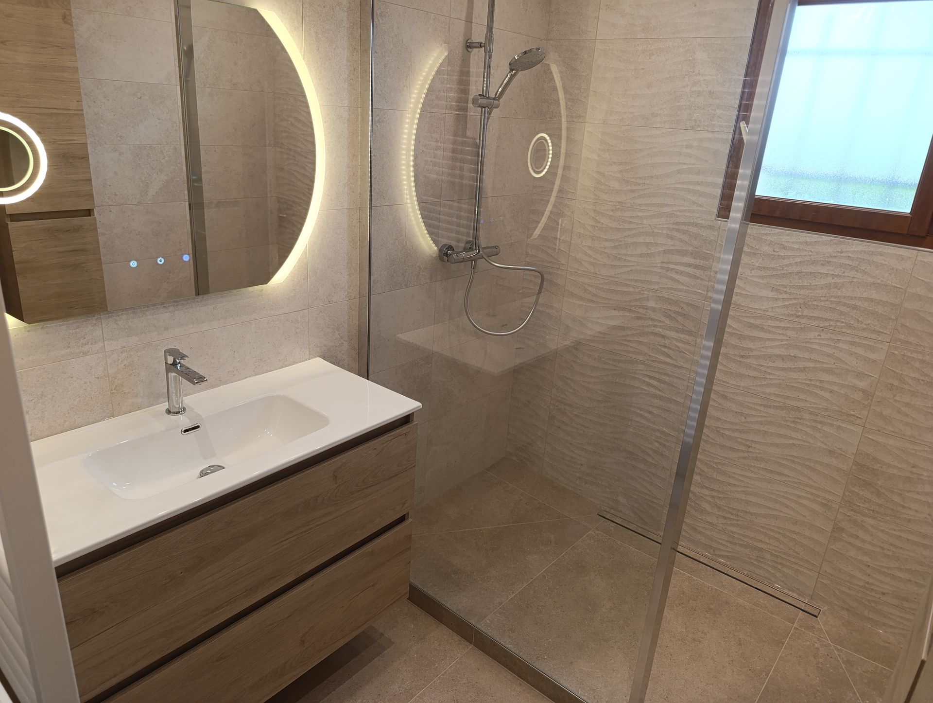 Salle de bains au design moderne : meuble-lavabo en bois, douche en verre et miroirs ronds éclairés.