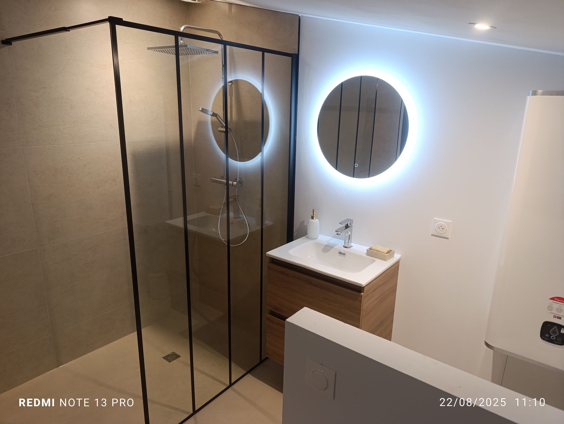 Salle de bains moderne avec douche en verre, miroirs ronds avec éclairage et meuble-lavabo en bois.
