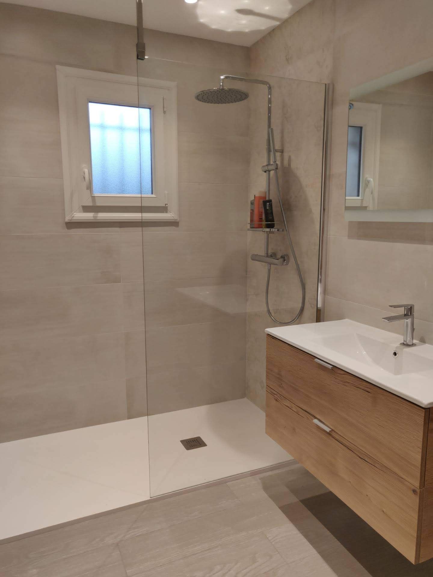 Salle de bains moderne avec douche à l'italienne, meuble-lavabo en bois et fenêtre. Palette de couleurs neutres et claires.