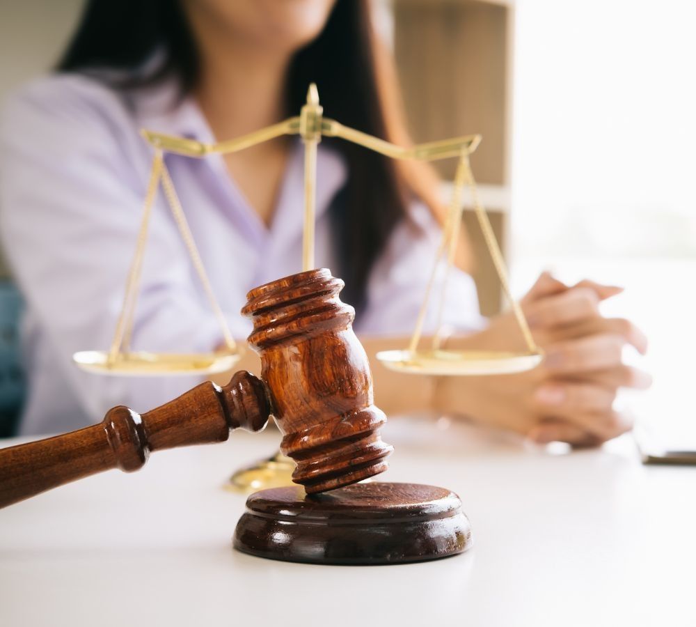 Una mujer está sentada en una mesa con un mazo de madera y una balanza de la justicia.