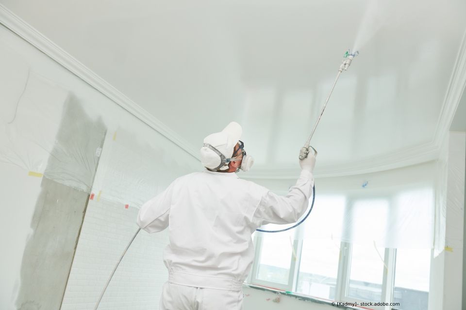 Decken wird gestrichen, Maler mit Farbsprühsystem sprüht Decke an