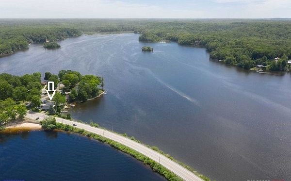 Aerial view of a Croton Pond with a road and buildings along the shoreline, surrounded by trees.