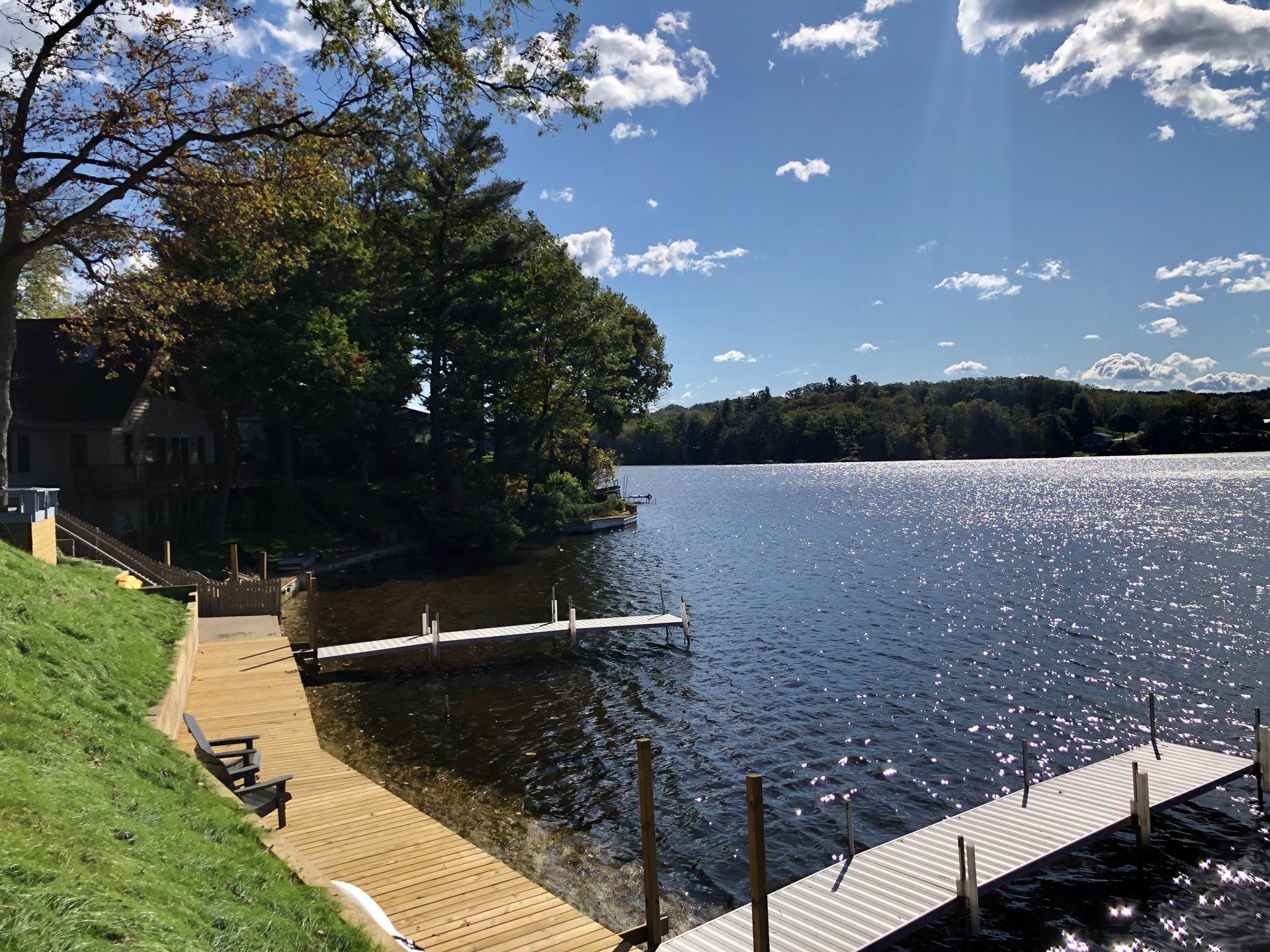 Lakeside view of docks and shoreline with trees and a blue sky. Water shimmers in the sunlight.