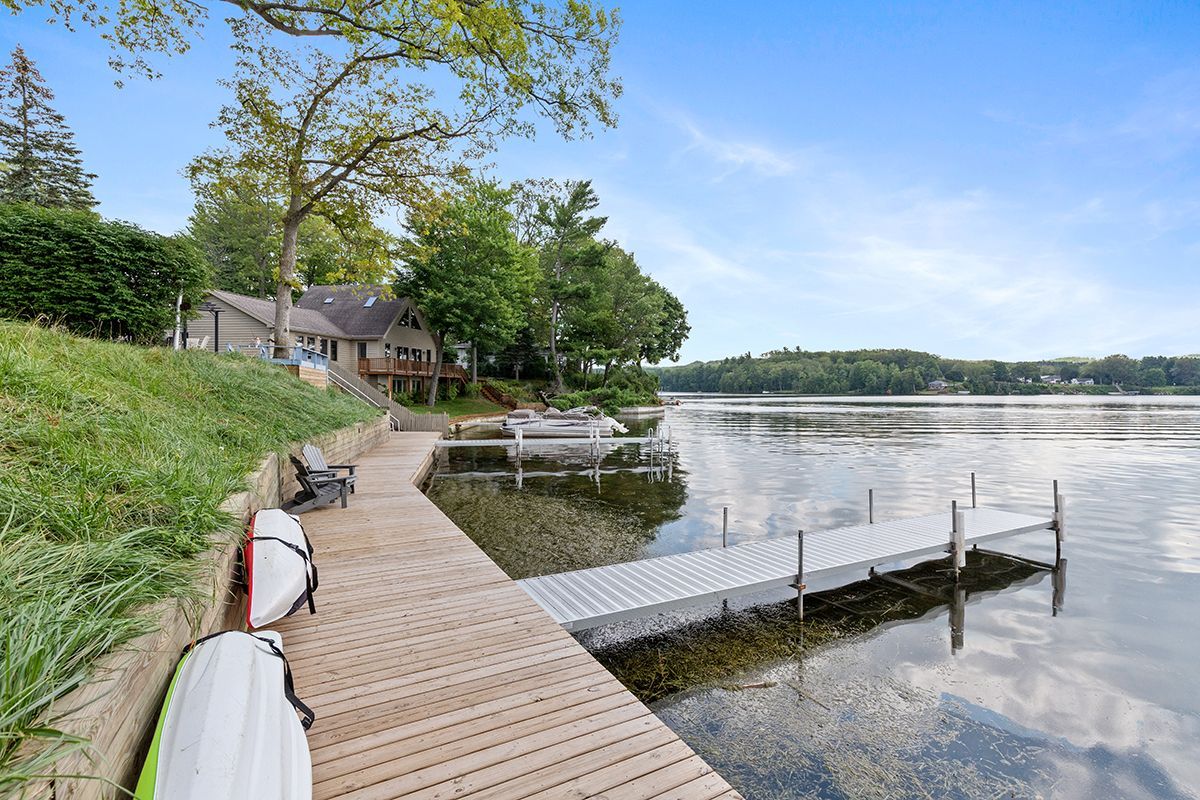 Our lakeside boardwalk with wooden dock and kayaks, overlooking calm water and trees under a blue sky.