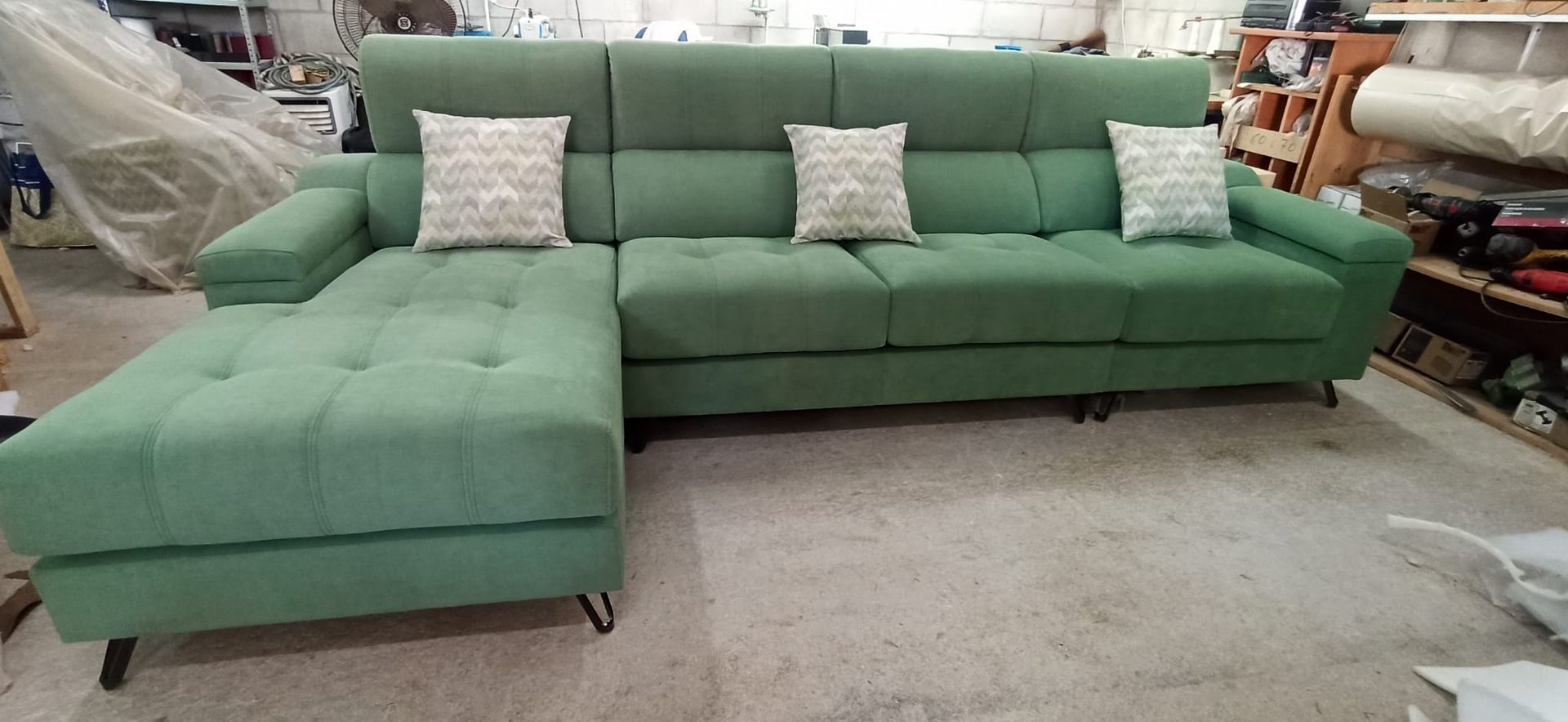 Sofá seccional verde en forma de L con chaise longue y cojines estampados en la sala de exposición de una tienda de muebles.