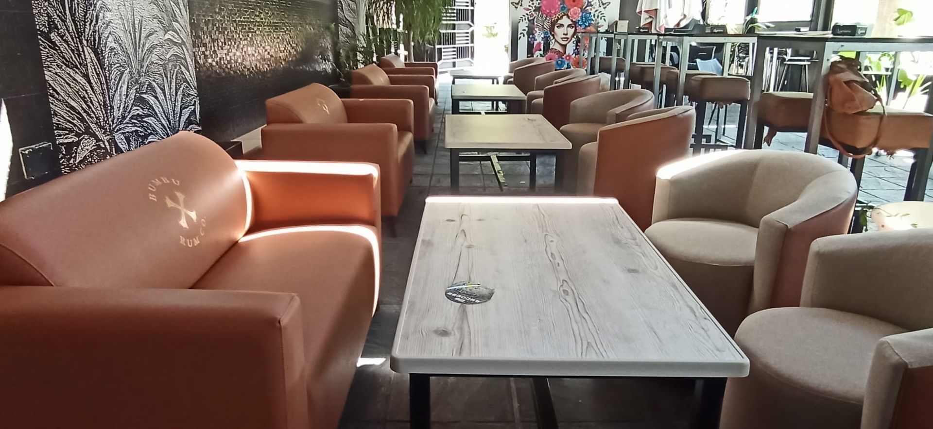 Cafetería vacía con sillones color canela y mesas de mármol sobre un suelo alfombrado.