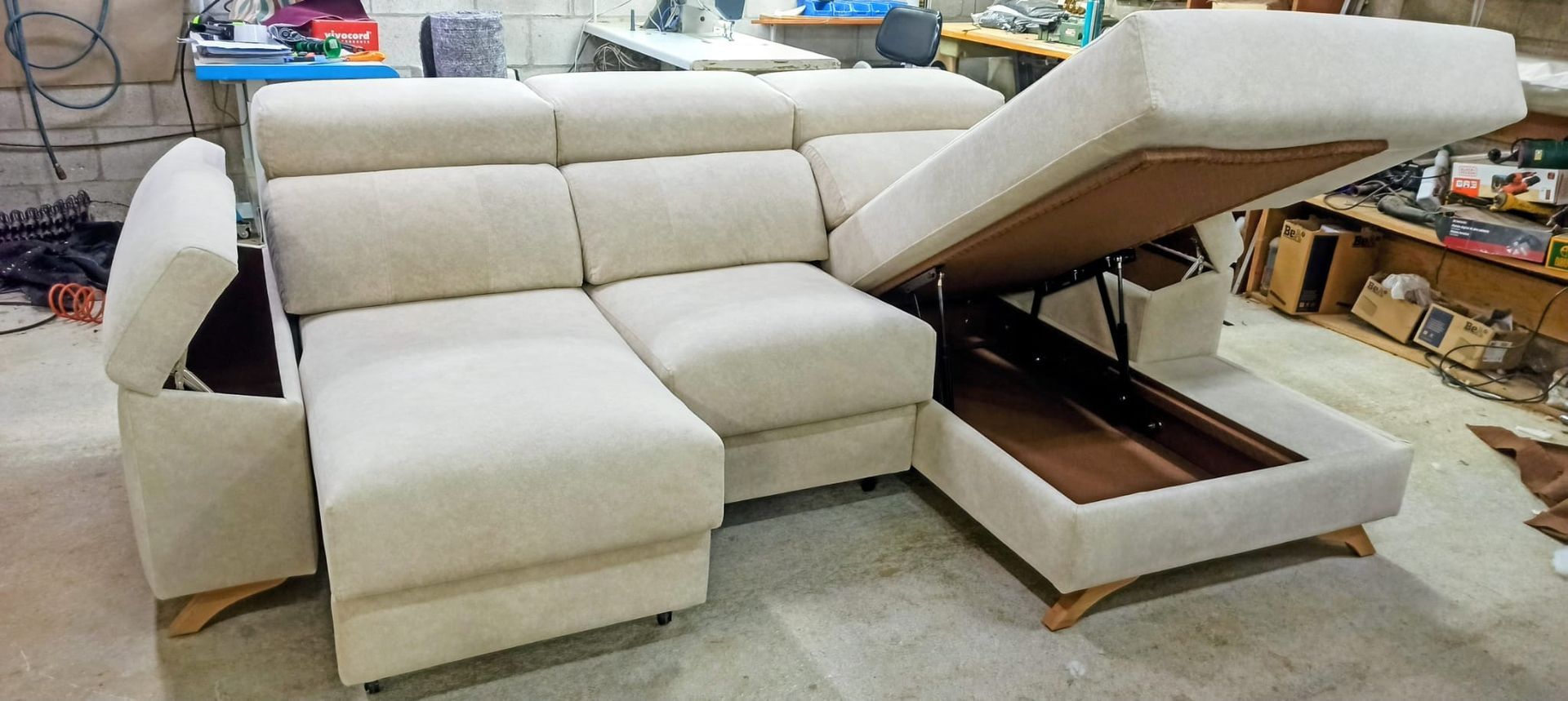Sofá modular de color beige en un taller, con la chaise longue levantada para revelar un espacio