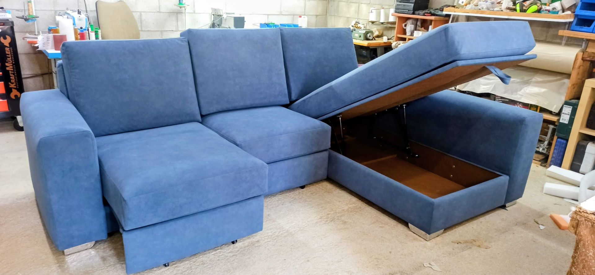 Sofá modular azul con chaise longue con espacio de almacenamiento y otomana abierta en una exposición de muebles.