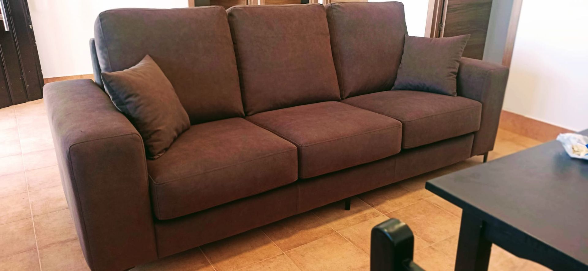 Sofá marrón en una sala de estar junto a una mesa de centro negra sobre un suelo de madera.