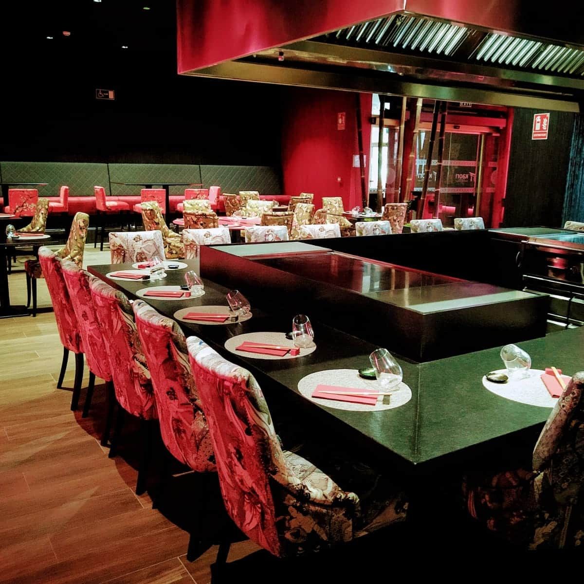 Elegante comedor teppanyaki con una gran mesa negra y sillas tapizadas en rojo bajo iluminación roja.