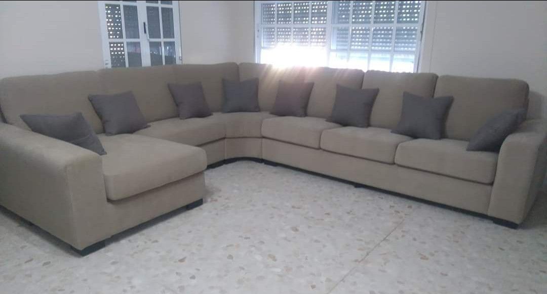 Sofá modular beige con cojines decorativos oscuros en una sala de estar luminosa cerca de una ventana.