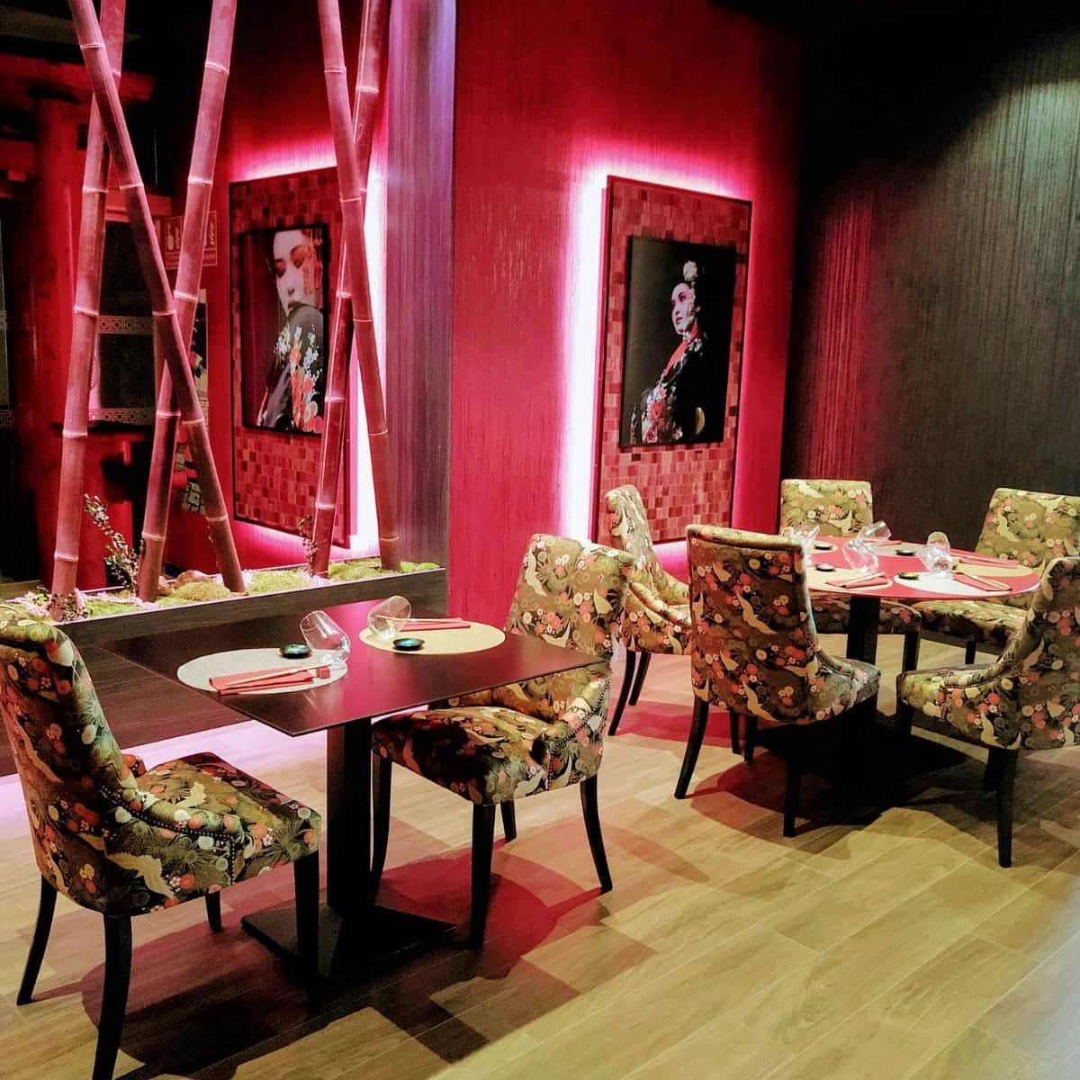Elegante comedor rojo con sillas y mesas decoradas con motivos florales, iluminado por una cálida luz ambiental.