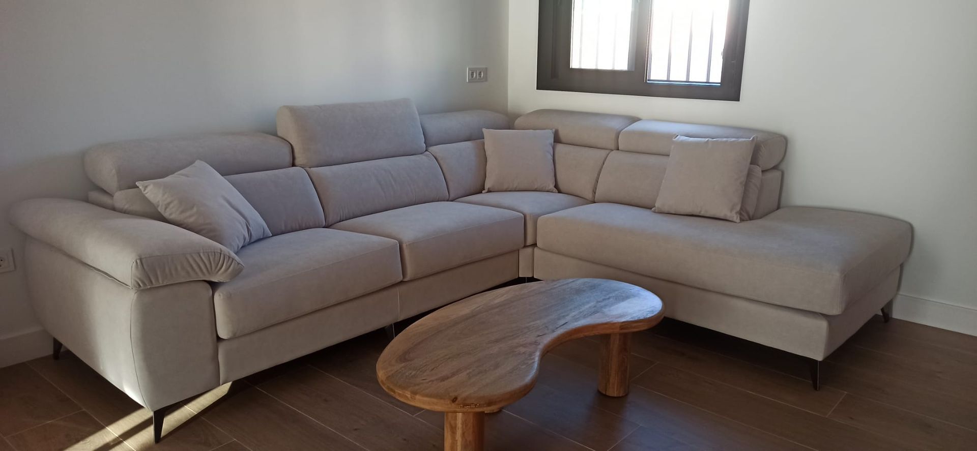 Sofá modular beige en una sala de estar luminosa con una mesa de centro de madera y luz de ventana.