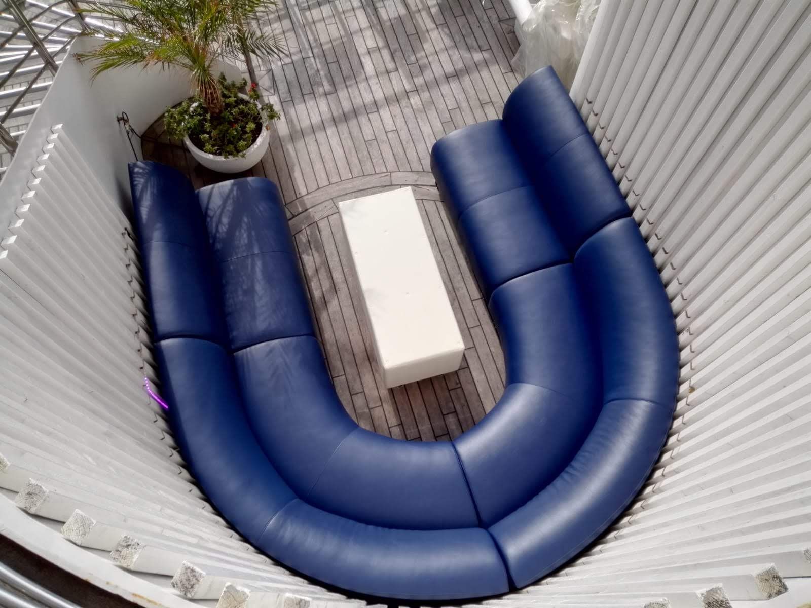 Sofá azul en forma de U para exteriores alrededor de una mesa blanca en un patio, visto desde arriba.