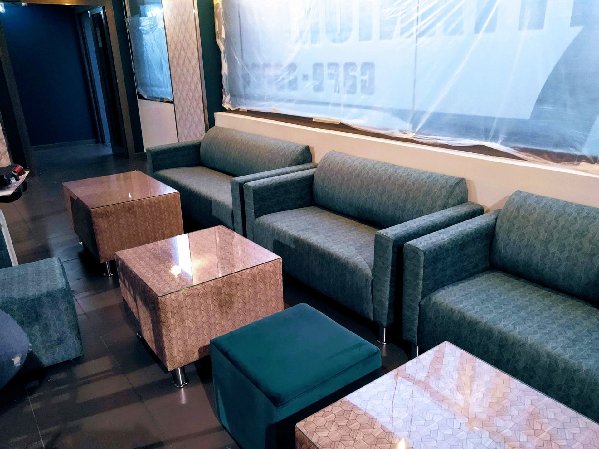 Salón vacío con sofás oscuros y mesitas junto a un escaparate esmerilado.