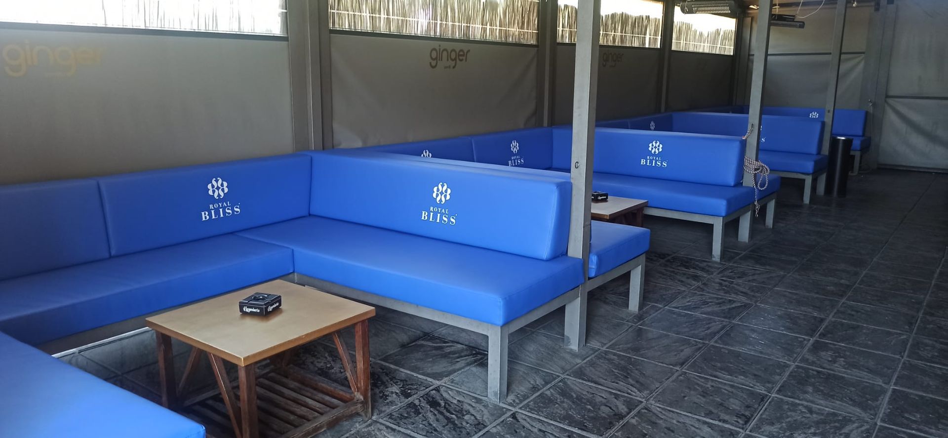 Asientos de exterior acolchados de color azul y una mesa pequeña bajo un área de patio cubierta.