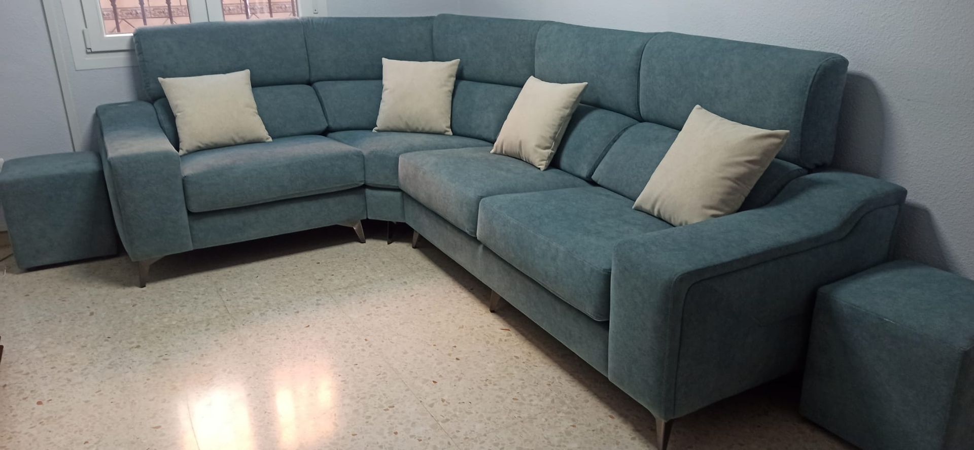 Sofá modular azul con cojines beige en una habitación con suelo moteado.