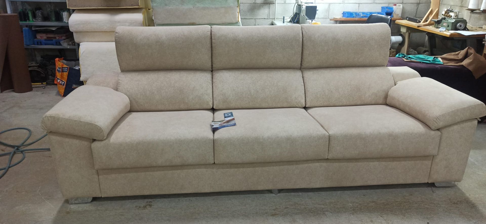 Sofá beige de tres plazas con respaldo reclinable en la sala de exposición de una tienda de muebles.